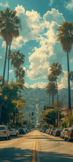 palm trees line the street in front of a blue sky with white clouds and mountains