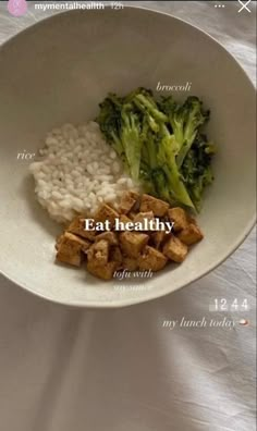 a white bowl filled with rice, broccoli and tofu on top of a table