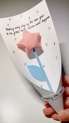 a hand holding an origami star on top of a piece of paper that says happy new year