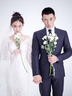 a man and woman holding flowers standing next to each other in front of a white background