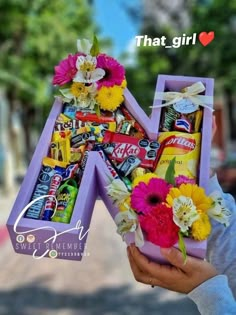 a person holding up a letter made out of candy and flowers