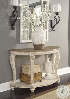 a white vase sitting on top of a wooden table next to a mirror and lamp