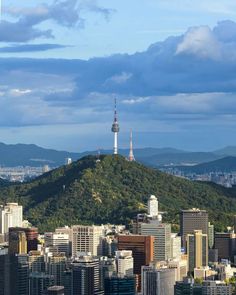 a city with tall buildings and a mountain in the background, under a cloudy blue sky