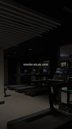 an empty gym room with treadmills and exercise equipment in the dark, while people watch on television