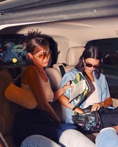 two women sitting in the back seat of a car looking at an open book and magazine