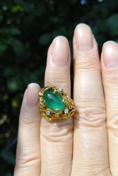 a close up of a person's hand wearing a ring with an emerald stone