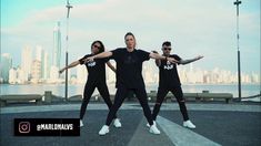 three men in black t - shirts and white sneakers are standing on the street with their arms outstretched