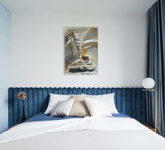 a bed with white pillows and blue headboard in a bedroom next to a painting on the wall