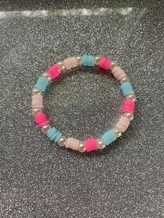 a pink and blue beaded bracelet sitting on top of a gray counter next to a bottle