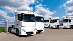 several white trucks parked in a parking lot with blue sky and fluffy clouds behind them