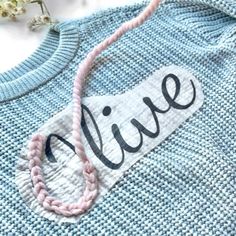 a blue sweater with the word alive on it and a pink beaded necklace hanging from it