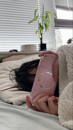 a woman laying in bed with her cell phone up to her face and holding it