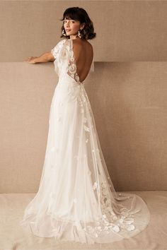 a woman in a white wedding dress with flowers on it's back, standing against a wall