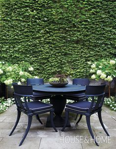 an outdoor table with four chairs and a bowl of flowers on it in front of a green wall