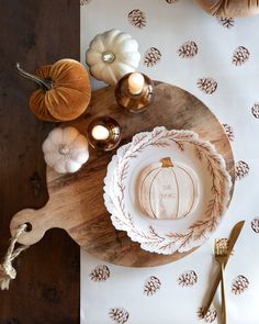 a wooden table topped with white plates and pumpkins next to gold candlesticks