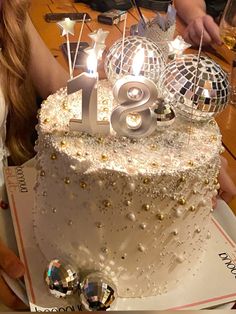 a white cake with silver numbers and disco balls on the top is surrounded by confetti