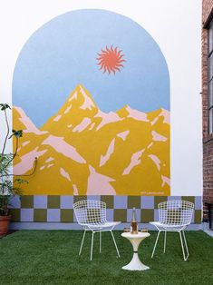 two white chairs sitting on top of a lush green field next to a wall mural