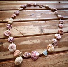 a necklace with seashells on it sitting on a wooden table next to a piece of wood