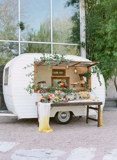 a white trailer parked in front of a building with plants growing out of the back