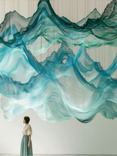 a woman is standing in front of a sculpture made out of blue and white waves