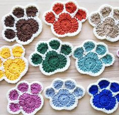 several crocheted paw prints are arranged on a wooden surface in different colors and sizes