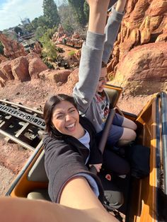 two people riding in a roller coaster at a theme park with mountains and rocks behind them