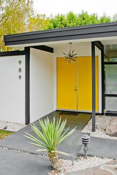 a yellow door sits in front of a white and black house with gravel around it