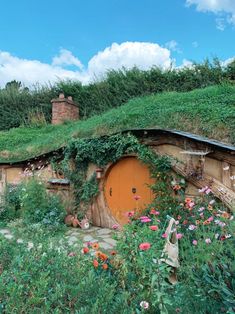 an old hobbot with flowers and plants growing on it's roof, in the middle of a field