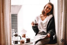 a woman sitting on a window sill holding a coffee cup