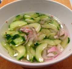 a white bowl filled with cucumbers and onions on top of a wooden table