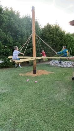 three children are playing on a wooden swing set in the backyard with grass and trees