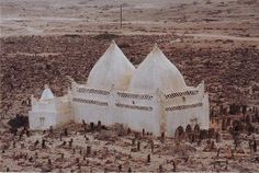 an old white building sitting in the middle of a barren area with trees and rocks