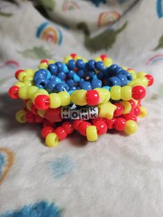 Step right up and add a splash of fun to your look with the Clowncore Rotator Cuff! Made with 30 vibrant beads and measuring 7 inches in length, this cuff bursts with bold red, yellow, and blue primary colors, inspired by the whimsical world of clowns. In the center, it proudly says "Honk," capturing the lighthearted, quirky vibe, while a cute smiley face charm adds an extra dash of cheer. Perfect for anyone who loves eye-catching accessories, this cuff is sure to make you the star of the show wherever you go! Clown Bracelet, Clowncore Kandi, Pony Bead Projects, Clown Clothes, Cute Smiley Face, Pony Bead Patterns, Rotator Cuff