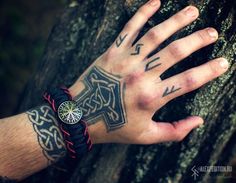 a man's hand with tattoos on it next to a tree