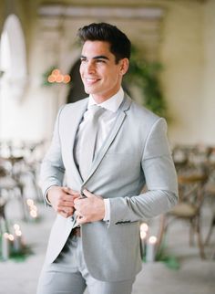 a man in a gray suit and tie standing next to tables with candles on them