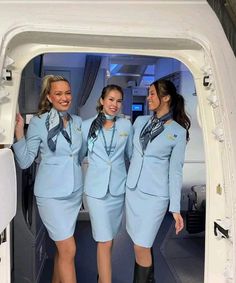 three beautiful women in blue uniforms standing on an airplane cabin door, with one holding her hand up to the side