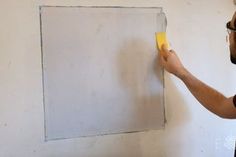 a man is painting the wall with white paint and yellow adhesivement on it