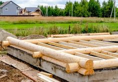 a house being built with wooden beams in the foreground and green grass behind it