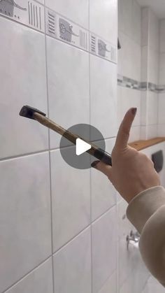 a person holding up a toothbrush in front of a bathroom wall with white tiles