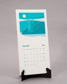 a desk calendar with an image of a lighthouse in the background on a black stand