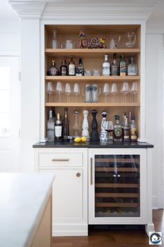 a white kitchen with wine glasses and bottles on the shelves above the bar area is filled with liquor