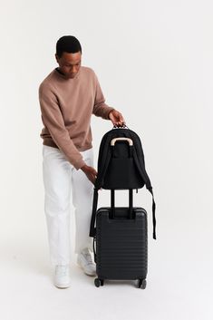 a man with a backpack on top of a rolling suitcase