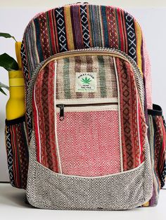 a colorful backpack sitting on top of a table next to a vase with a plant in it