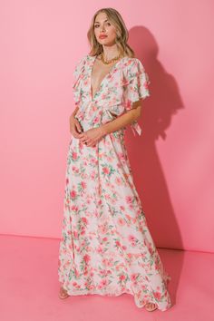 a woman standing in front of a pink wall wearing a floral dress