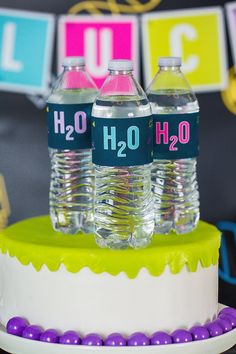 two water bottles sitting on top of a cake with purple and green decorations around it