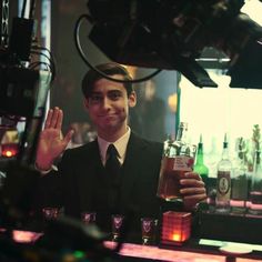 a man in a suit and tie holding up a bottle of alcohol at a bar