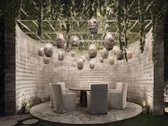 an outdoor dining area with white chairs and greenery hanging from the ceiling above it