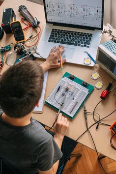 a man sitting at a desk working on a laptop computer surrounded by electronic components and wires