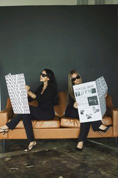 two women sitting on a couch holding papers