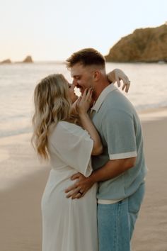 a man and woman standing on the beach kissing each other with an ocean in the background